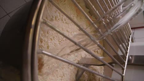 vertical slow motion shot of a large dough mixer or spiral mixer preparing delicious pizza dough while water is being added