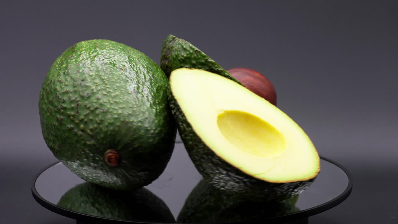 Close up shot of 3 avocados rotating on a mirror and a black background