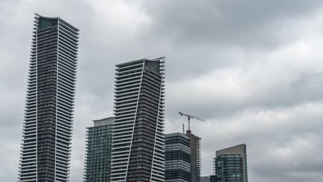 Clouds-over-skyscrapers-and-construction-in-Toronto,-tilt-up-timelapse