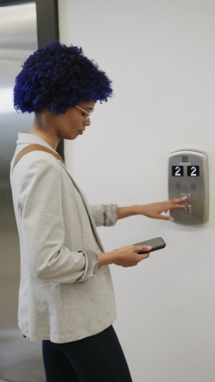 Video verticale di donna d'affari birazziale informale che usa uno smartphone e l'ascensore, al rallentatore.