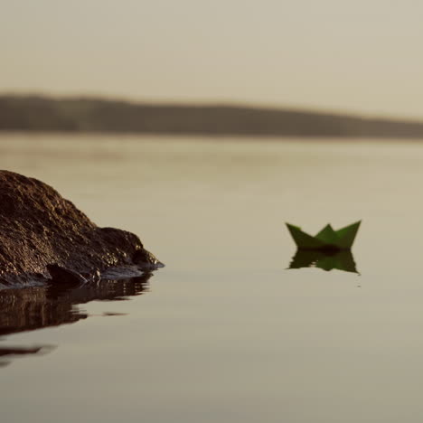 green paper ship in the river. origami paper boat is sailing in the lake. beautiful waves ripple background. unusual travel concept. filtered video.