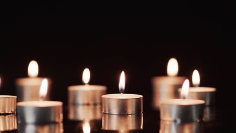 Video-of-rows-of-tea-candles-with-white-flames-and-copy-space-on-black-background