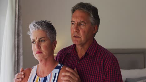 una pareja de ancianos caucásicos estresados hablando entre sí mientras miran por la ventana en casa