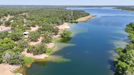 moving and turning left above a small lake inlet that has a public recreational area that has a beach area, boats, and fishing dock