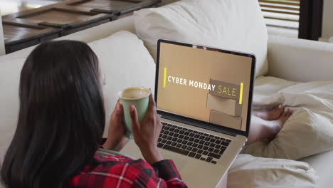 una mujer biracial usando una computadora portátil en casa comprando en línea en el día de venta del lunes cibernético, en cámara lenta