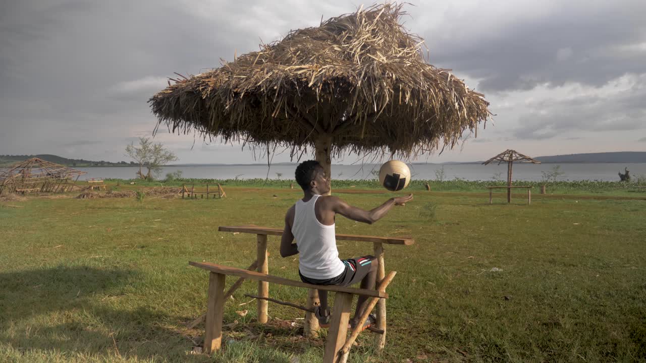 detrás de la foto de un joven africano relajándose en una cabaña en la playa a orillas del lago victoria mientras jugaba con una pelota de fútbol