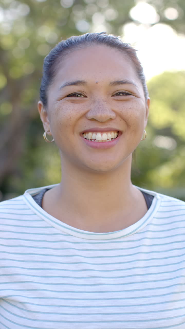 Vertical video: Smiling woman outdoors, enjoying sunny day in casual striped shirt