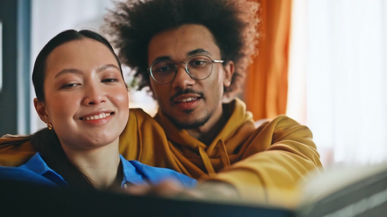 Closeup multiethnic couple browsing photo album home. Pair sharing memories