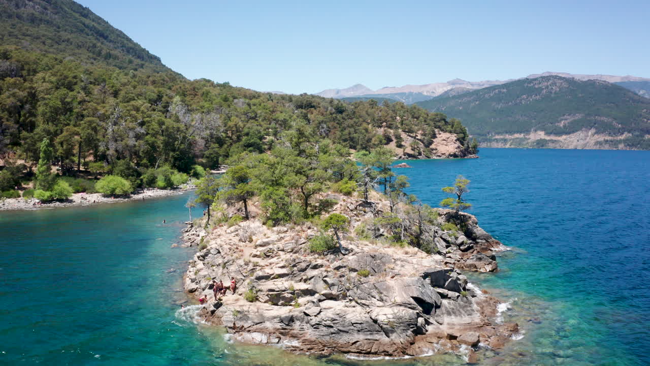 People jump into water from islet by hilly coast in Argentina, aerial
