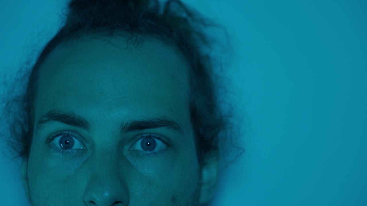 Portrait of a man with eyes closed under soft blue lighting, peaceful expression, static as he looks up staring forward