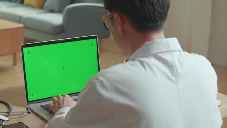 male doctor typing on laptop computer with green screen display at home office, video in 4k