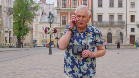 Älterer-Alter-Tourist-In-Stilvoller-Kleidung,-Der-Beim-Spazierengehen-Auf-Der-Stadtstraße-Mit-Dem-Mobiltelefon-Telefoniert