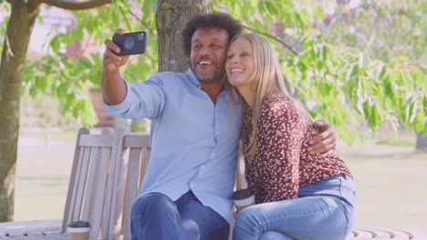 loving mature couple posing for selfie on mobile phone sitting on seat in park