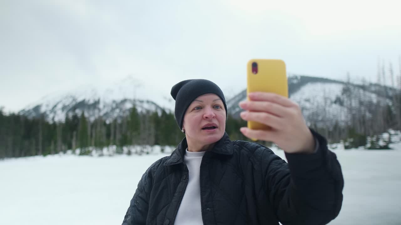 Woman taking selfie in snowy mountains by frozen lake