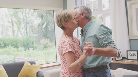 Romantic-Senior-Retired-Couple-Dancing-In-Lounge-At-Home-Together