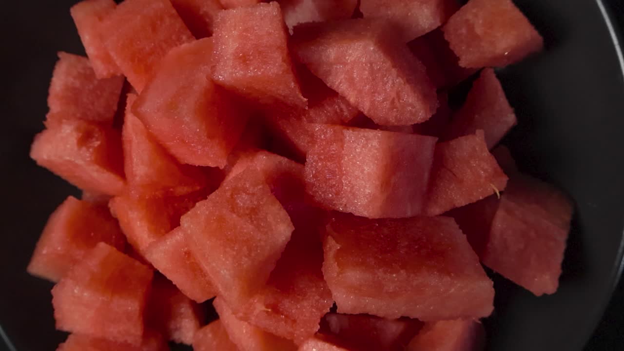 Top down video of colorful red and tasty watermelon cubes that are sliced into a dark colored bowl. video spins around over the tasty and healthy snacks smoothly
