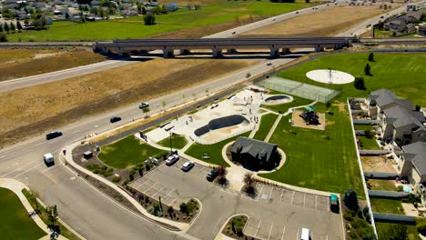 Orbiting-aerial-view-of-a-skate-park-between-a-highway-and-a-suburban-neighborhood