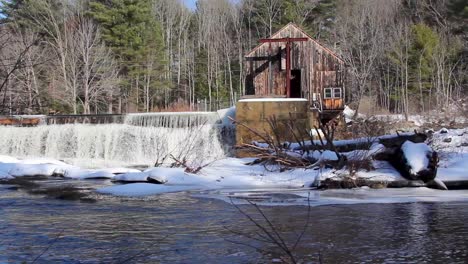rushing water pours over dam next to dilapidated building