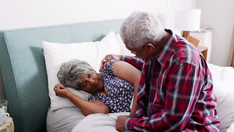 senior man comforting woman with depression lying in bed at home