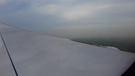 Aerial-view-from-airplane-window-showing-wing-and-clouds-with-landscape-below-during-descent