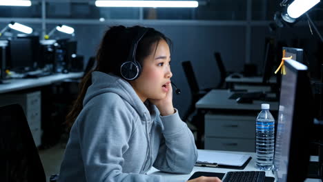 Woman wearing a headset working on a computer in a call center or office at night