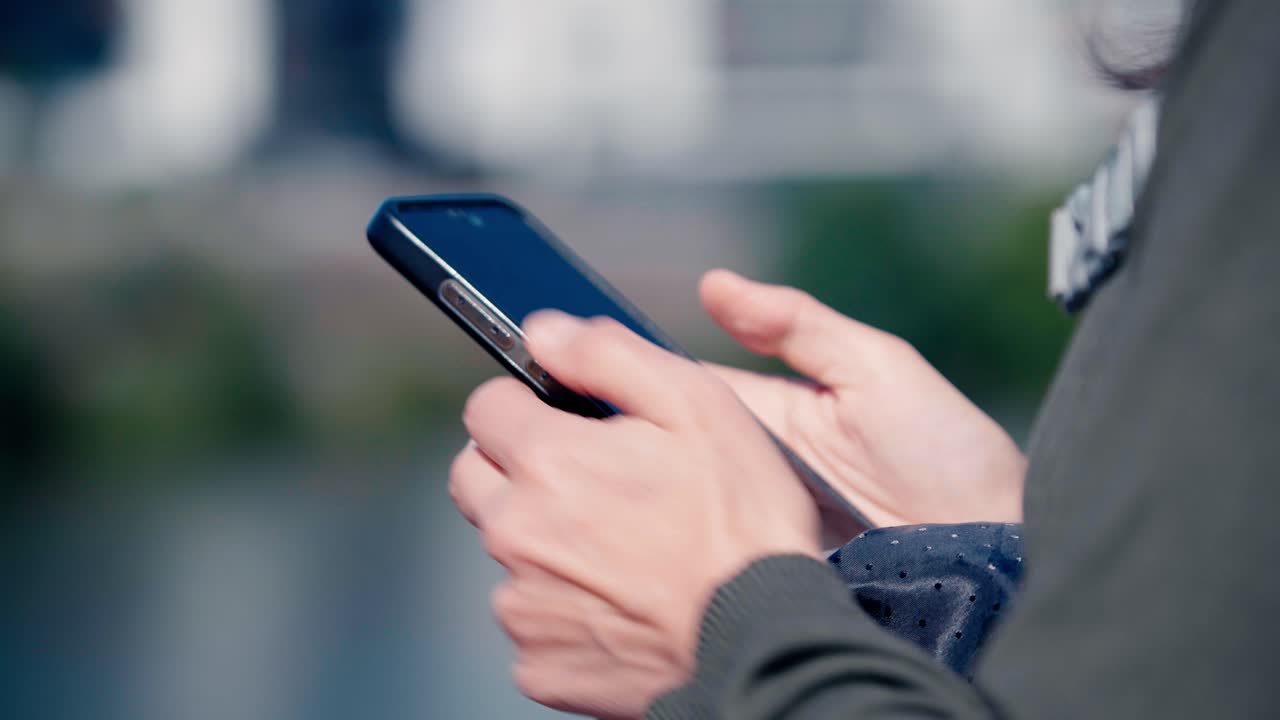 Primo piano di mani che stringono un telefono cellulare con lo schermo visibile. Uno sfondo urbano sfocato suggerisce un'ambientazione cittadina a Nantes durante il giorno.