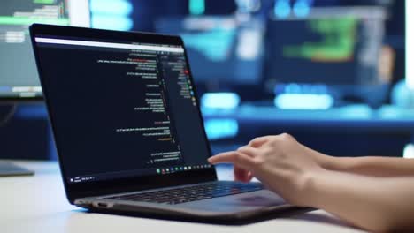 a focused programmer engaged in coding with an open laptop displaying lines of code in a dimly lit environment with multiple screens in the background