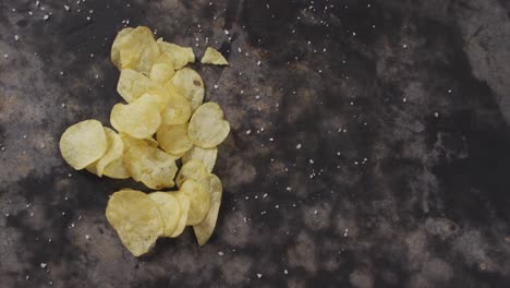 close up view of salt over potato chips with copy space on black surface