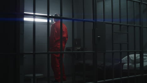 elderly prisoner in orange uniform holds hands on metal bars