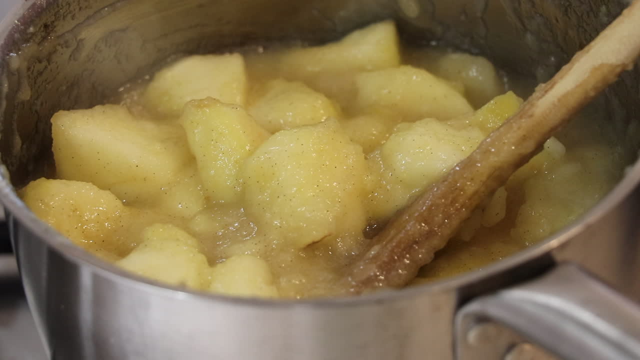 primer plano de manzanas para cocinar espolvoreadas con canela molida, guisadas en una sartén, burbujeando suavemente con vapor saliendo y una cuchara de madera utilizada para revolver