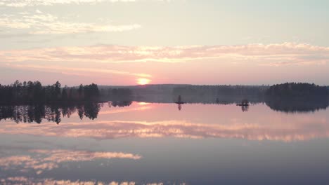 Aerial-view-of-a-perfectly-mirrored-lake-in-a-forest-during-autumn-and-sunset