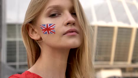 portrait of a young blonde girl soccer fan of england looking into the camera, smiling, serious face, stadium in the background 50 fps