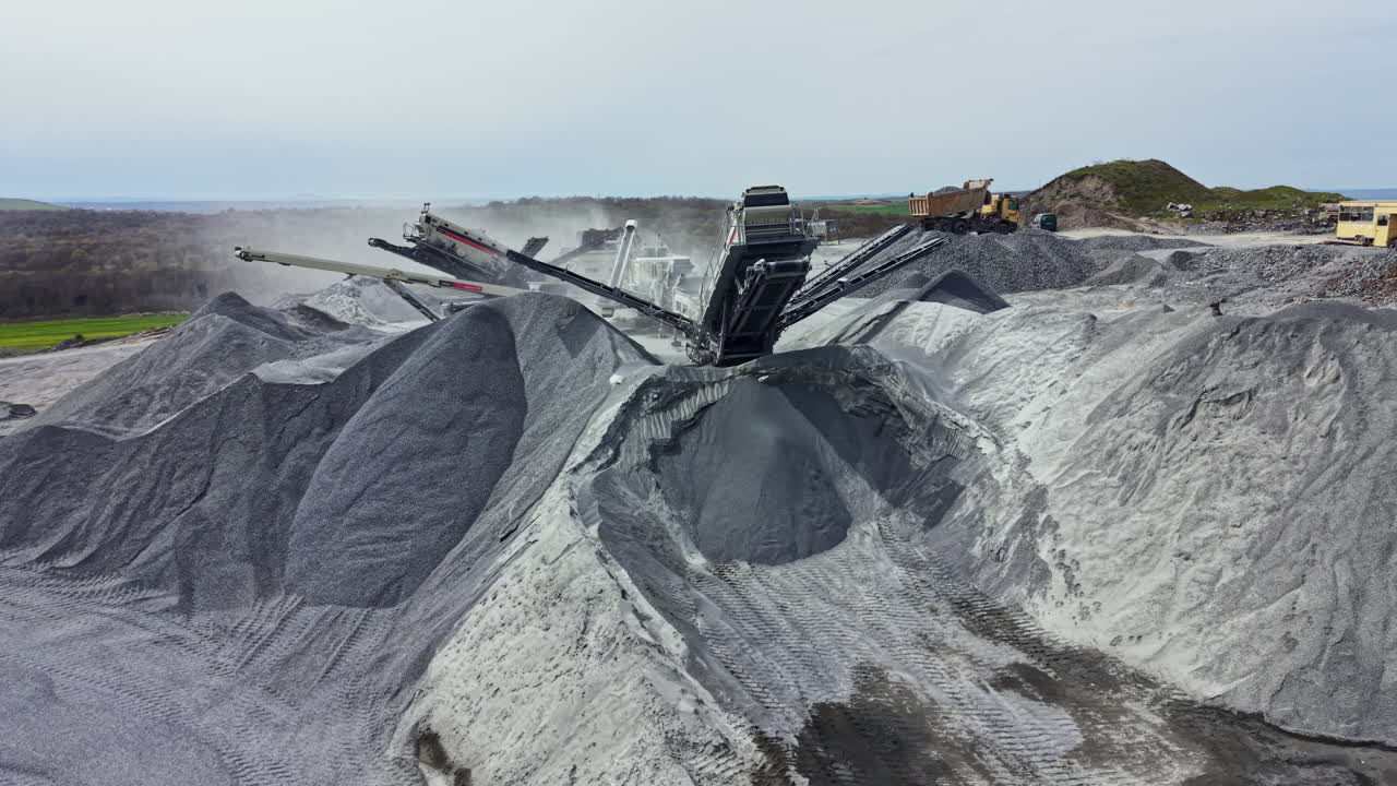 Granite quarry operation with heavy machinery and stone piles under cloudy sky in recent afternoon