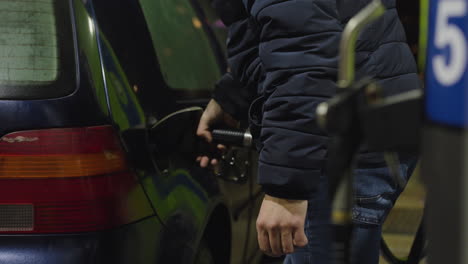 hombre bombea gasolina en un coche azul oscuro compacto en una noche fría de invierno, gasolinera en primer plano