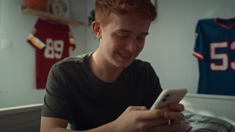 Close-up-of-caucasian-teenage-boy-browsing-phone-while-sitting-in-his-bedroom