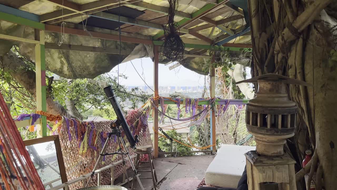 An eclectic hideaway adorned with colorful decorations and a telescope, offering a unique perspective of Honolulu's skyline through lush foliage.
