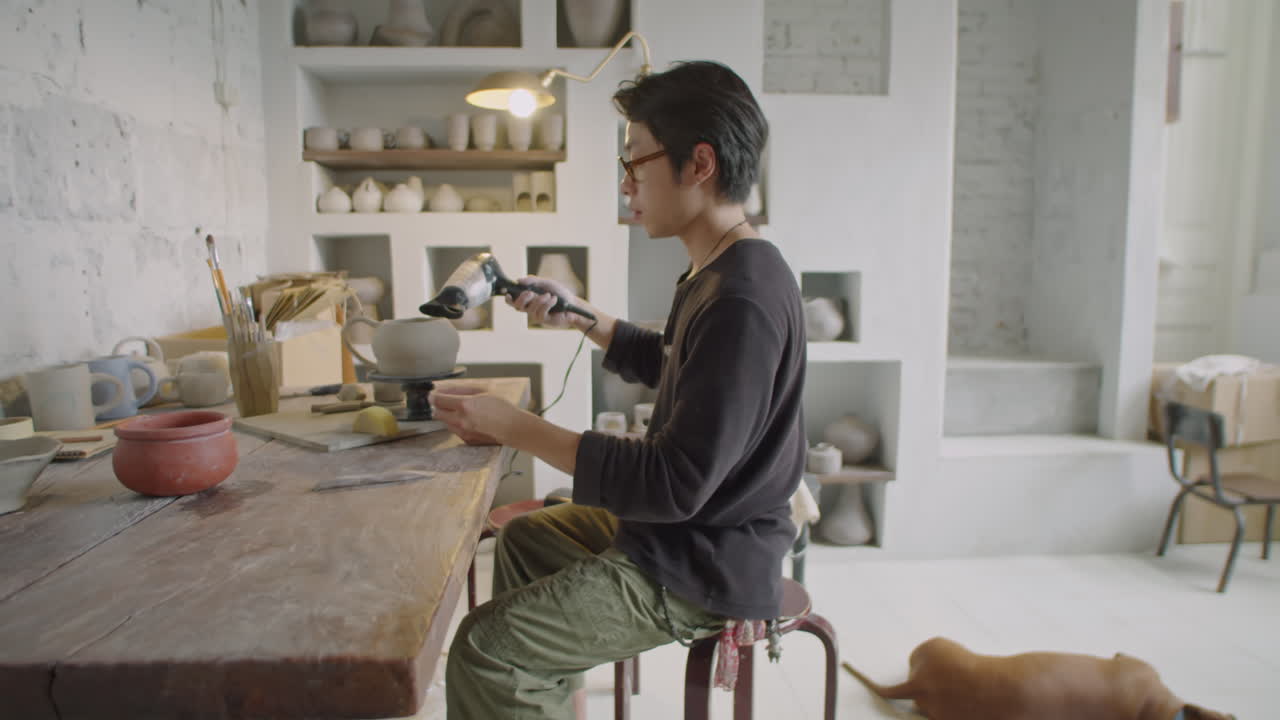 Asian Ceramist Drying Mug on Pottery Wheel with Hairdryer