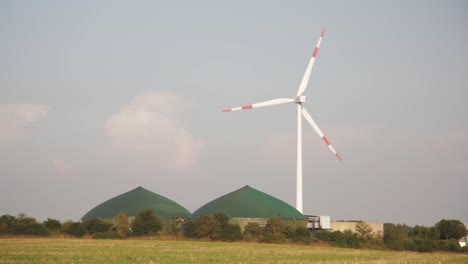 wide shot of spinning windmill with bio gas facility