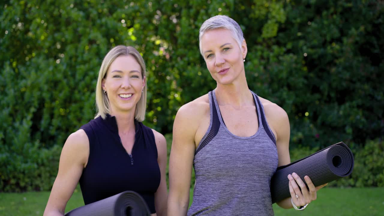 Freundinnen halten Yogamatten auf dem Rasen, lachen, lehnen sich nach Armübungen und bereiten sich auf das Training vor.