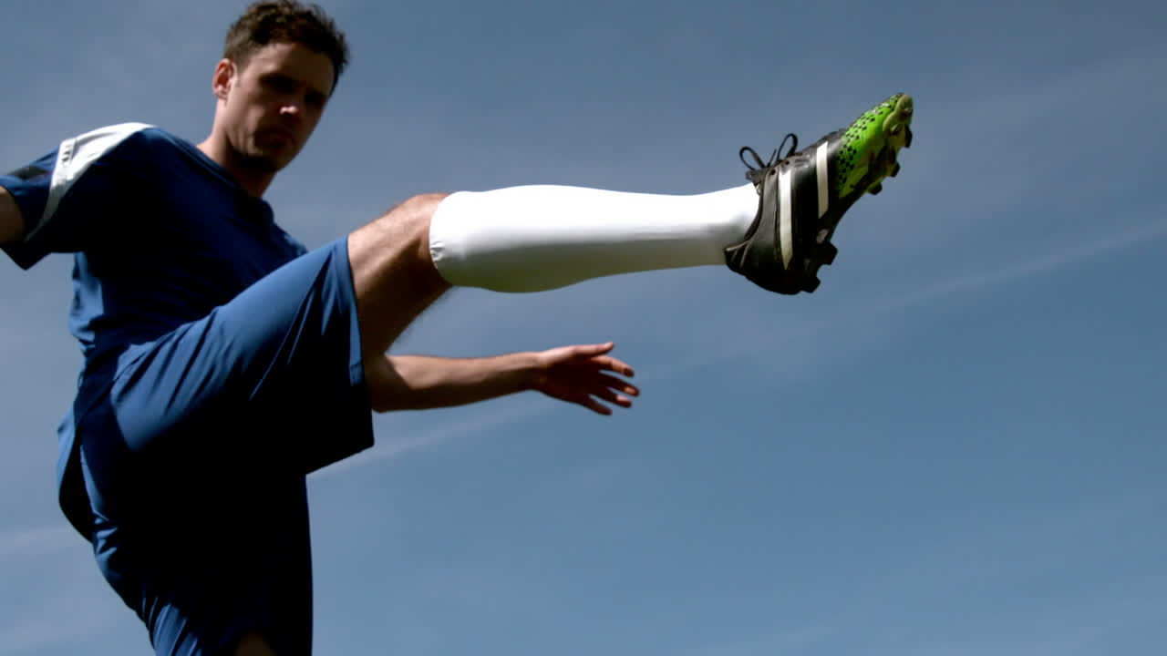 Football player kicking the ball up under blue sky