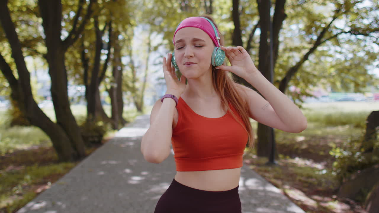 corredora deportiva chica bonita entrenamiento ejercicio escuchar música en auriculares bailar divirtiéndose en el parque