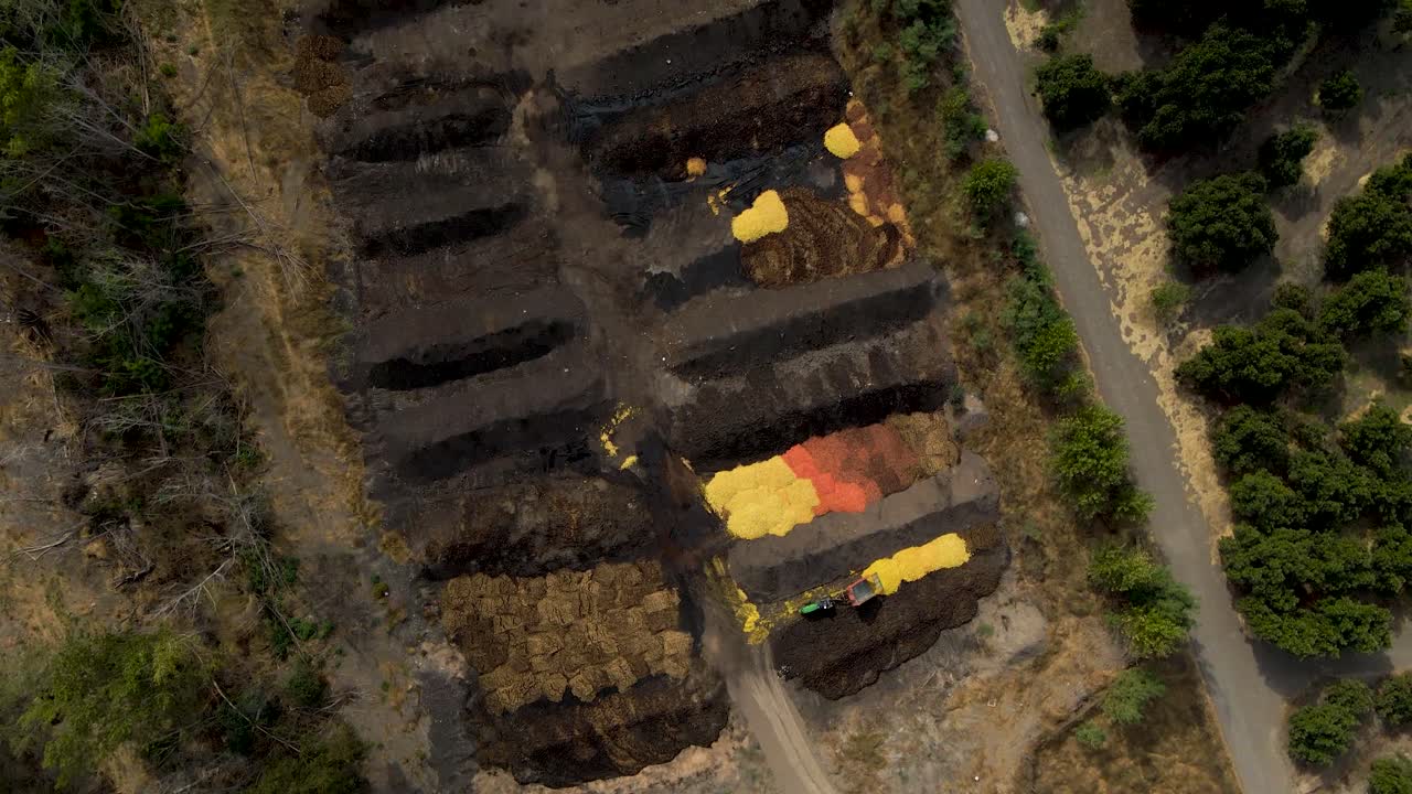 Aerial top down dolly in of a tractor discarding orange shells in a compost area surrounded by plantations in a farm field at daytime