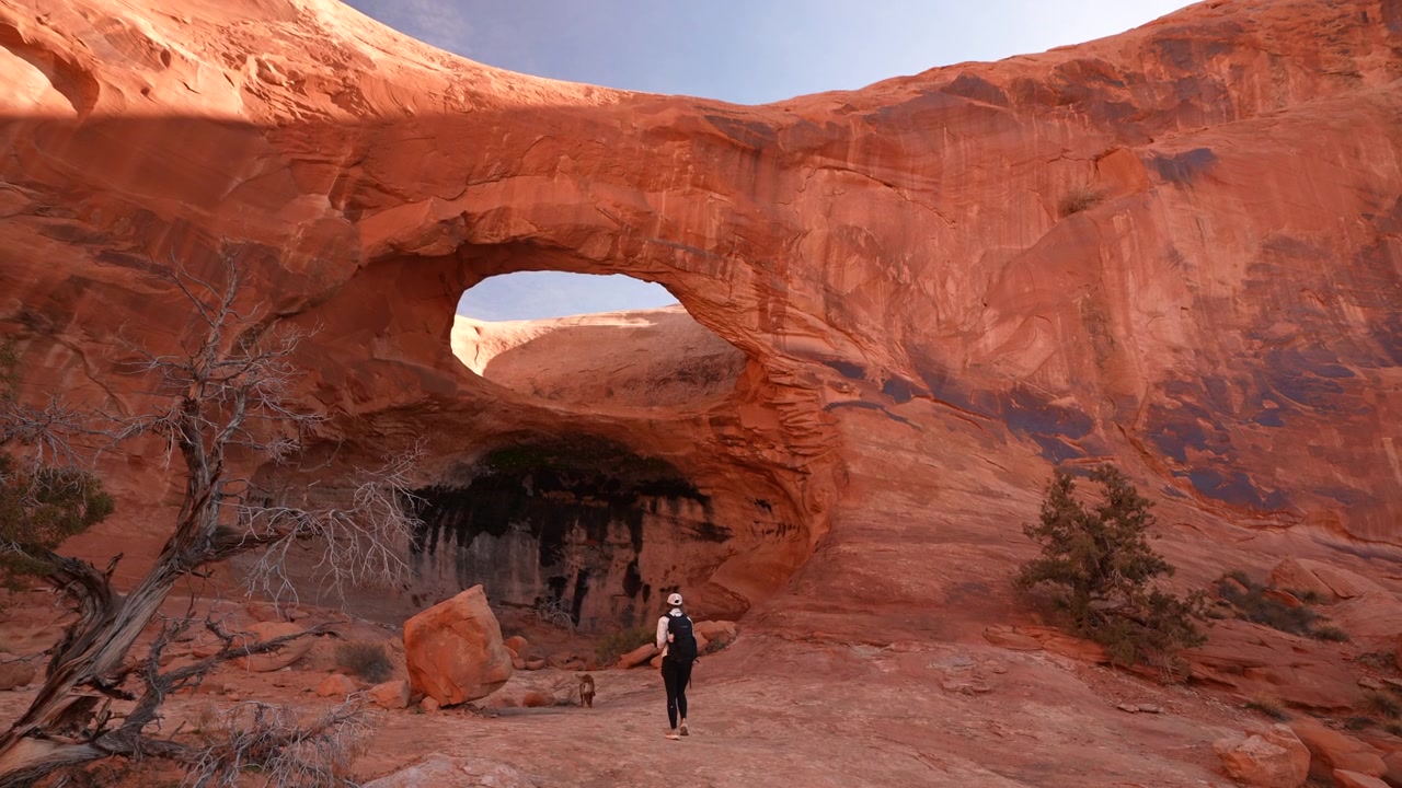Donna e cane sotto l'Arco Pinto, attrazione naturale panoramica ed escursione da Moab, Utah, USA