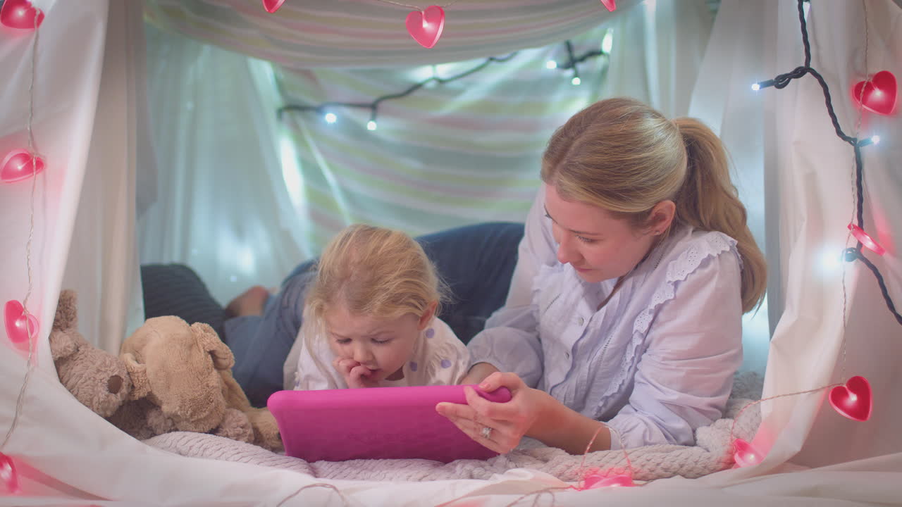 Mother and young daughter with digital tablet in homemade camp in child's bedroom at home - shot in slow motion