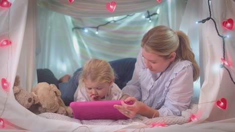 Mother-and-young-daughter-with-digital-tablet-in-homemade-camp-in-child's-bedroom-at-home---shot-in-slow-motion