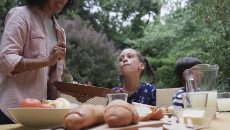 Happy biracial mother, son and daughter enjoying meal at dinner table in garden, slow motion