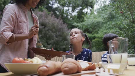 happy biracial mother, son and daughter enjoying meal at dinner table in garden, slow motion