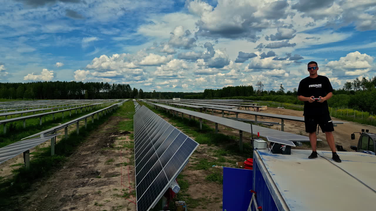 un hombre pilotando un drone por encima de los paneles solares en una gran granja solar - drone volando hacia adelante