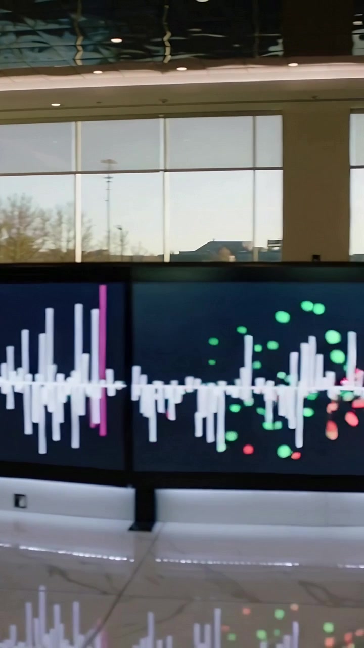 Video verticale: Telecamera in panoramica, display a pannello curvo che mostra una forma d'onda bianca e particelle nella hall