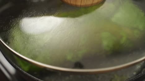 anonymous cook removing lid from frying pan with spinach omelette